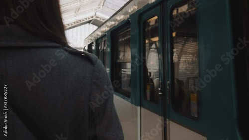 Rear view young woman walking along arriving metro train at Paris railway station platform, looking right slow motion. photo