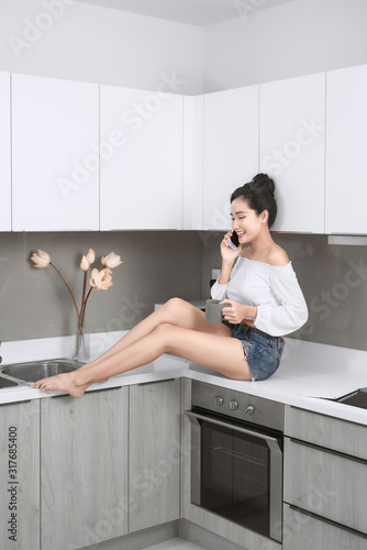 Sexy Asian woman talking by mobile phone while sitting in the kitchen.