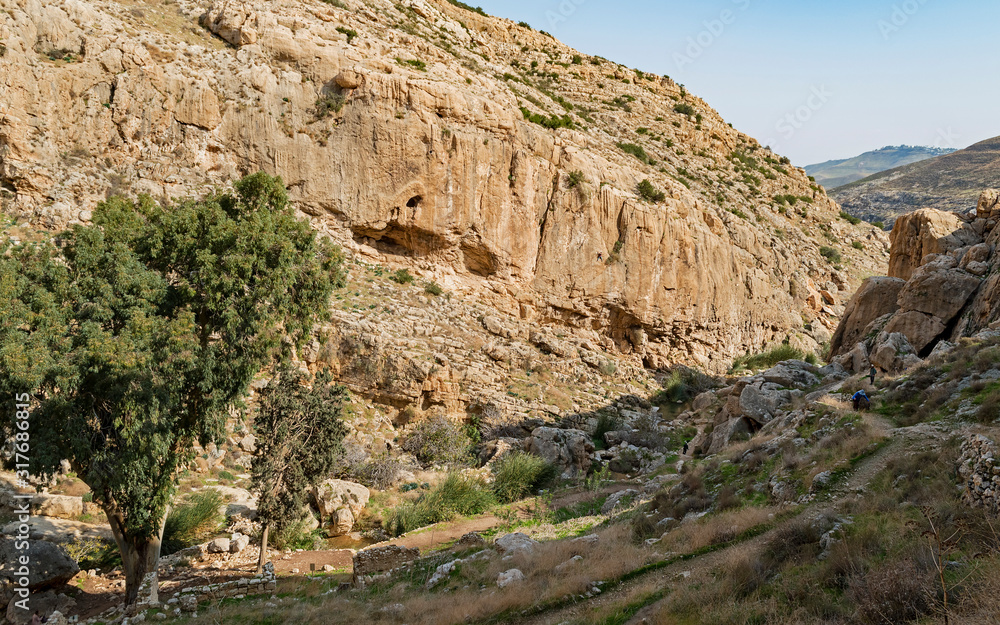hikers on the trail to the ancient faran monastery near ein prat in wadi qelt in the west bank with ruins of a church and aqueduct  in the foreground