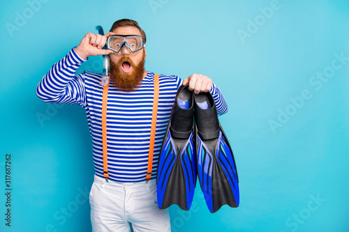 Surprised amazed redhair man impressed coral reef relax resort sport hold flippers have breathing mask tube goggles wear white shorts orange suspenders isolated blue color background photo