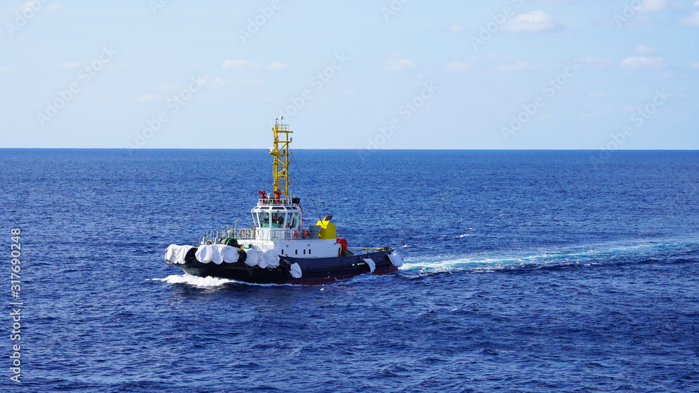 A bright, powerful industrial tugboat cuts through the sea waves on a sunny day. mole tugboat floating in the blue water of the Pacific Ocean pushing a big wave A bright, powerful industrial tugboat cuts through the sea waves on a sunny day. mole tugboat floating in the blue water of the Pacific Ocean pushing a big wave
