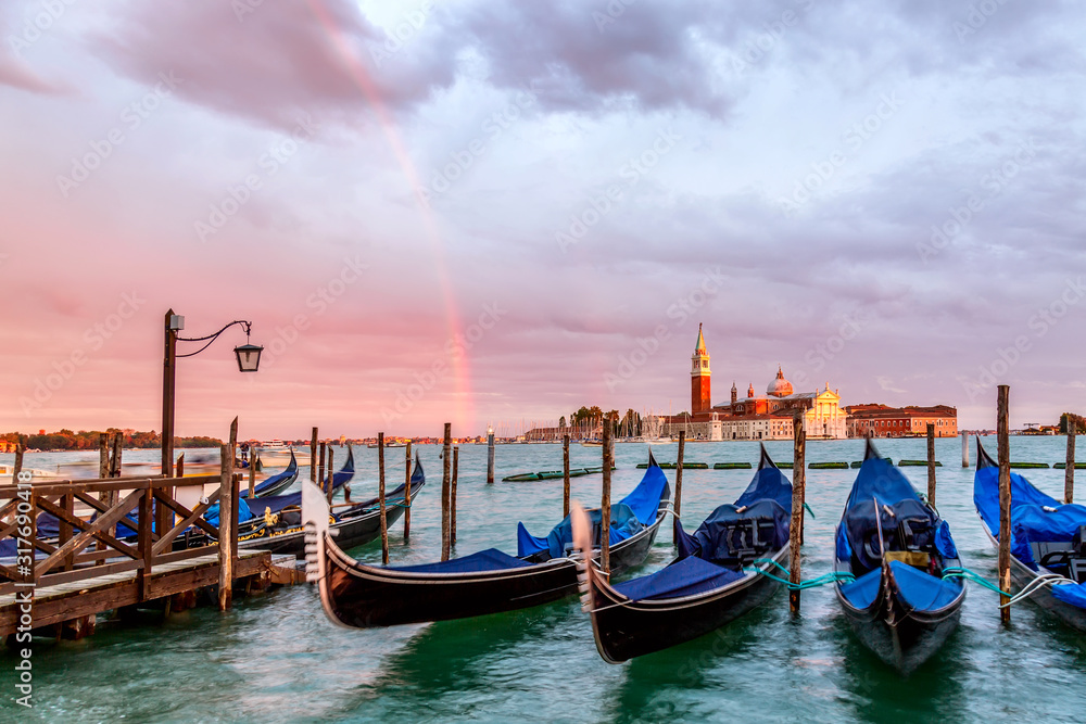 Colorful landscape with sunset sky, rainbow and gondolas parked near piazza San Marco in Venice. Church of San Giorgio Maggiore on background, Italy. Europe tourism concept.