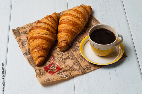 Espresso coffee in vintage yellow cup and saucer, croissants on craft paper, on a light background, breakfast concept