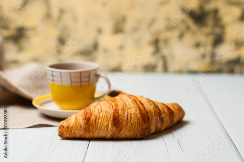 Espresso in vintage yellow cup with saucer and spoon, on linen napkin croissant on light background, concept of lunch
