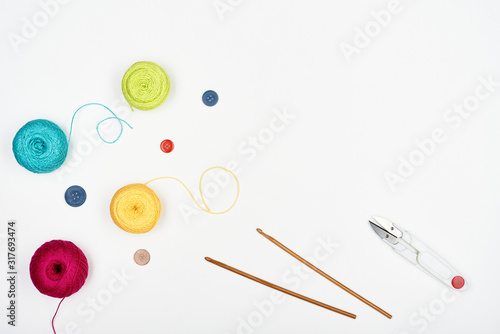 Colored threads and buttons, scissors and crochet hooks on a white background.