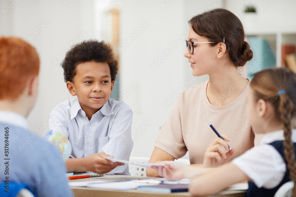 Young teacher sitting at the table together with her students and they doing homework in team at school Young teacher sitting at the table together with her students and they doing homework in team at school