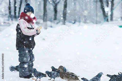 child playing in the snow / the girl in warm sports clothes is playing with snow on a winter walk. Warm woolen hat, down jacket. Concept of a happy baby walk.