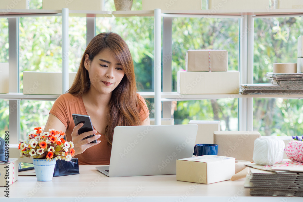 Beautiful Asian businesswoman holding a smartphone and looking at a laptop while sitting in the office Beautiful Asian businesswoman holding a smartphone and looking at a laptop while sitting in the office