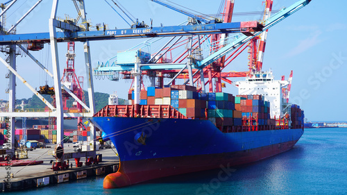 A huge container ship in the cargo terminal of an Asian port in Taiwan. Port container cranes load a moored barge with multi-colored containers. worldwide shipping by sea