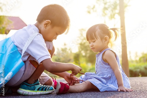 Soft focus. A young Asian brother help his little sister to tie her shoelaces. At the garden park in sunshine day summer season. Love and family concept. photo