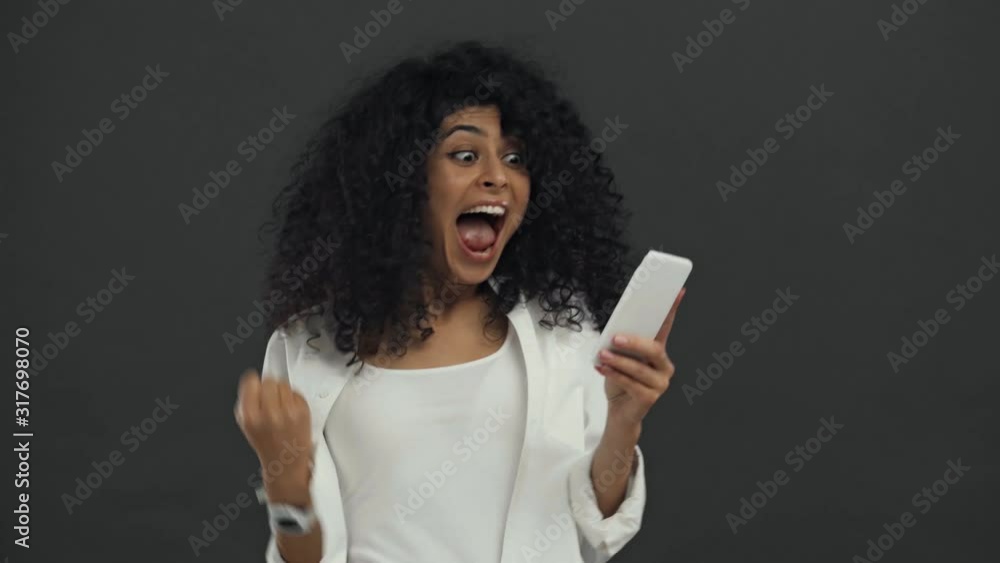happy bi-racial woman with smartphone celebrating triumph isolated on black happy bi-racial woman with smartphone celebrating triumph isolated on black