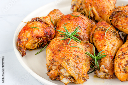 Close-Up Photo of Roast Chicken Pieces with Rosemary on a Plate on White Background.