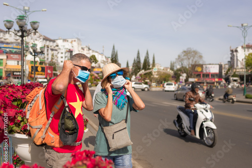 Woman and man wearing sanitary mask outdoors in Da Lat city centre Vietnam. Medical mask protection against risk of chinese flu virus epidemy in Asia. Anti smog mask traffic pollution.