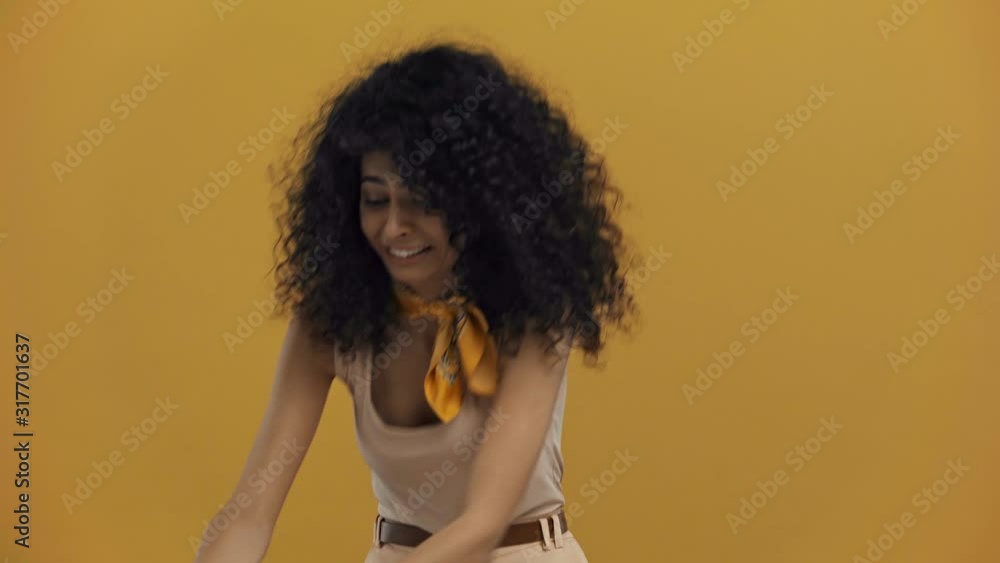 aggressive bi-racial woman breaking alarm clock isolated on dark yellow aggressive bi-racial woman breaking alarm clock isolated on dark yellow