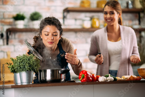 Two friends having fun in kitchen. Sisters cooking together.