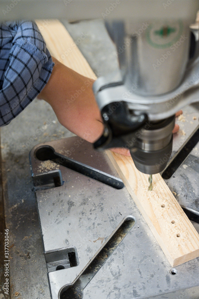 Eine Person bohrt mit einer Standbohrmaschine Löcher in ein Holzstück Eine Person bohrt mit einer Standbohrmaschine Löcher in ein Holzstück