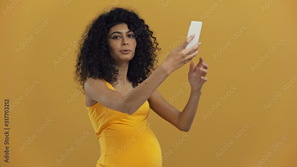 smiling bi-racial pregnant woman taking selfie isolated on dark yellow smiling bi-racial pregnant woman taking selfie isolated on dark yellow