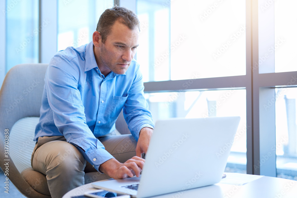 Serious businessman working on his laptop in bright office space