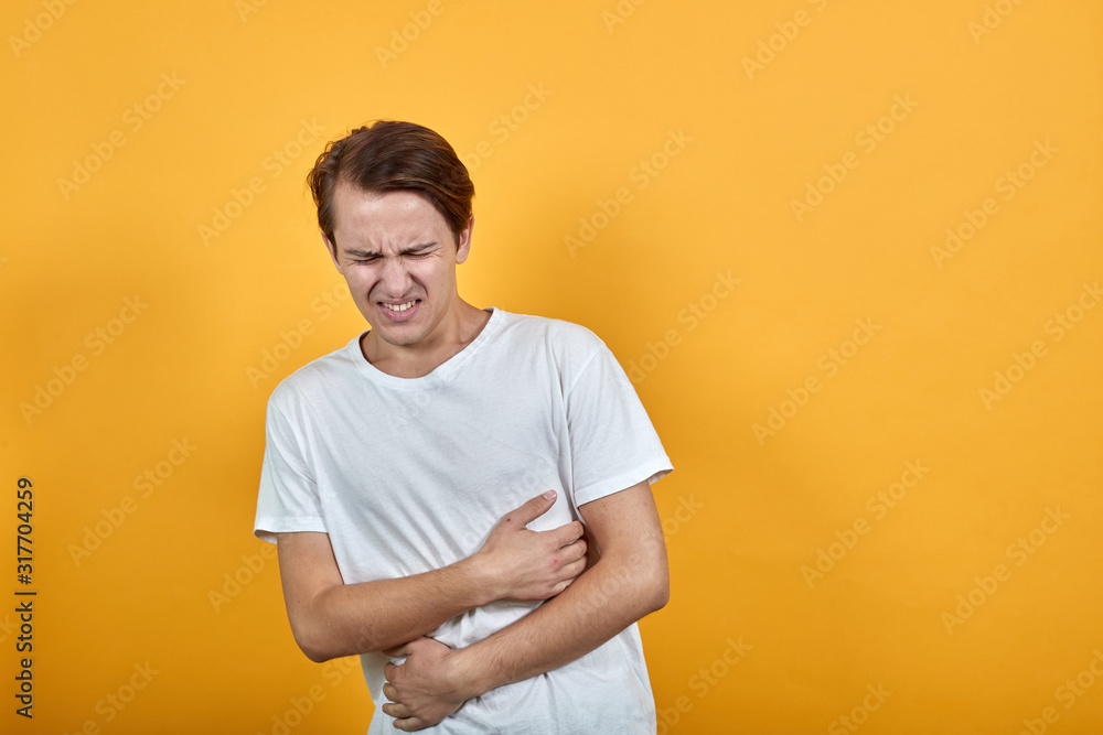 Man in a white t-shirt with abdominal pain health problem discomfort diarrhea yellow background Man in a white t-shirt with abdominal pain health problem discomfort diarrhea yellow background