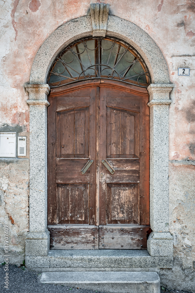 Wooden gray retro round arch door with rusty wrought iron lattice, gray plaster wall of the house Wooden gray retro round arch door with rusty wrought iron lattice, gray plaster wall of the house