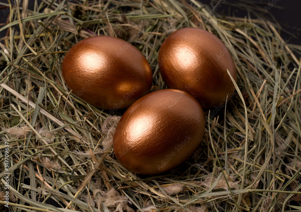 copper colored easter eggs on a black background in a nest of hay close-up. copper colored easter eggs on a black background in a nest of hay close-up.