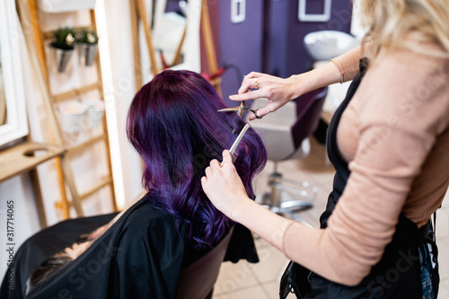 Beautiful hairstyle of young adult woman with purple hair in hair salon.