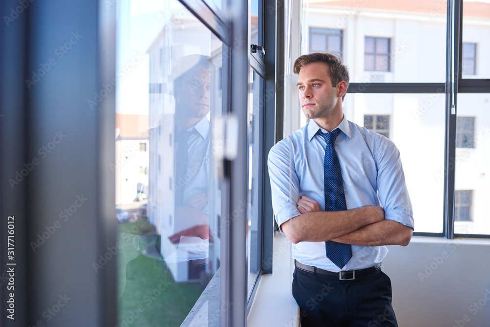 Fototapeta premium Young business achiever looking through window thinking about future