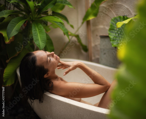 Fotografiet Woman relaxing in outdoor bath with tropical leaves at Bali