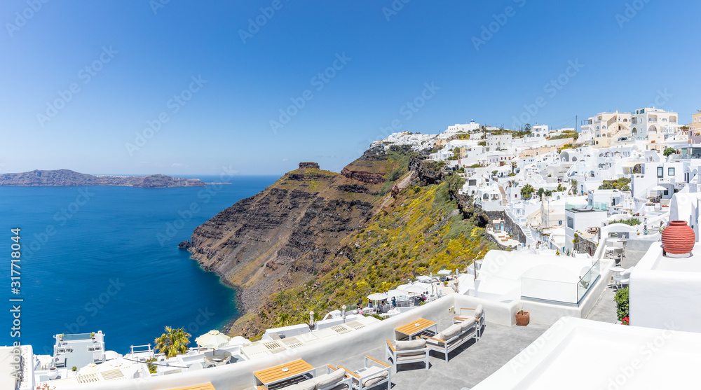  Santorini, Greece. Famous view of traditional white architecture Santorini landscape with flowers in foreground. Summer vacations background. Luxury travel tourism concept. Amazing summer destination