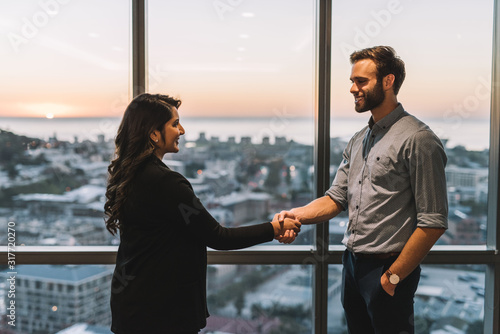 Smiling colleagues shaking hands by office windows overlooking the city photo