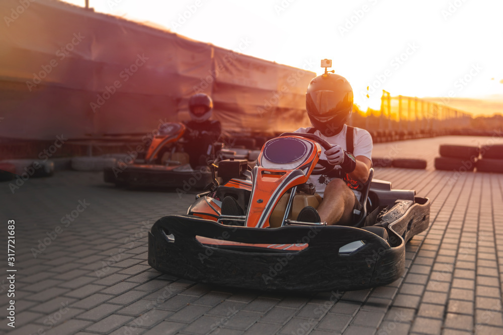 Naklejka premium Two racers on karts are approaching the finish line in an active battle for first place in the championship, sreet, rent. extreme sport. fun entertainment for drivers, sunset soft light