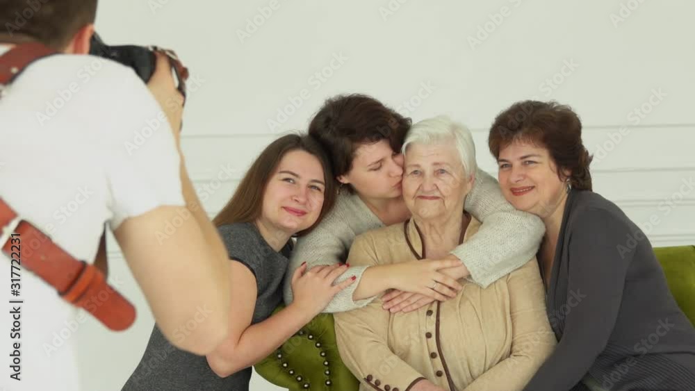 Photographer is taking pictures of an elderly white-haired woman with her granddaughters. The beautiful multi-generations family enjoys togetherness Photographer is taking pictures of an elderly white-haired woman with her granddaughters. The beautiful multi-generations family enjoys togetherness