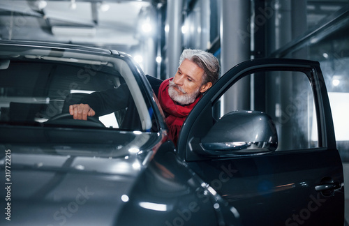 Stylish senior man with grey hair and mustache sitting into brand new modern car © standret