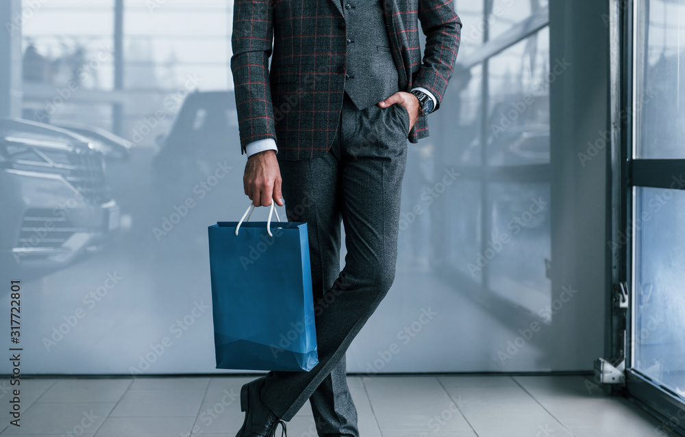 Close up view of businessman in suit standing indoors with blue package Close up view of businessman in suit standing indoors with blue package