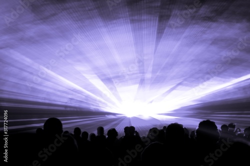 Purple laser show nightlife club stage with party people crowd. Luxury entertainment with audience silhouettes in nightclub event  festival or New Years Eve. Beams and rays shining colorful lights