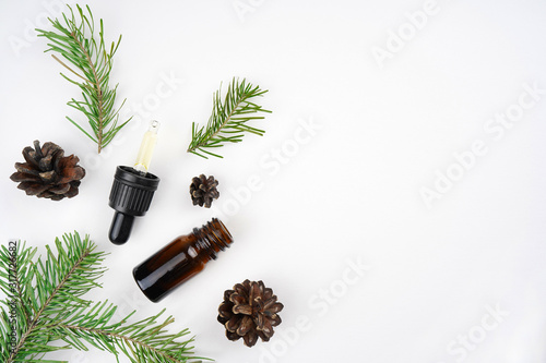 Pine aroma essential oil in brown bottle, fir branches and cones, white background. Spa, beauty, healthcare concept. Top view, flat lay, copy space