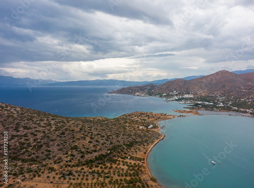 Mediterranean Sea from a height, coast of Crete, Greece. A boat in the azure waters of the bay, agricultural fields against the backdrop of the sea and mountains. Aerial shot