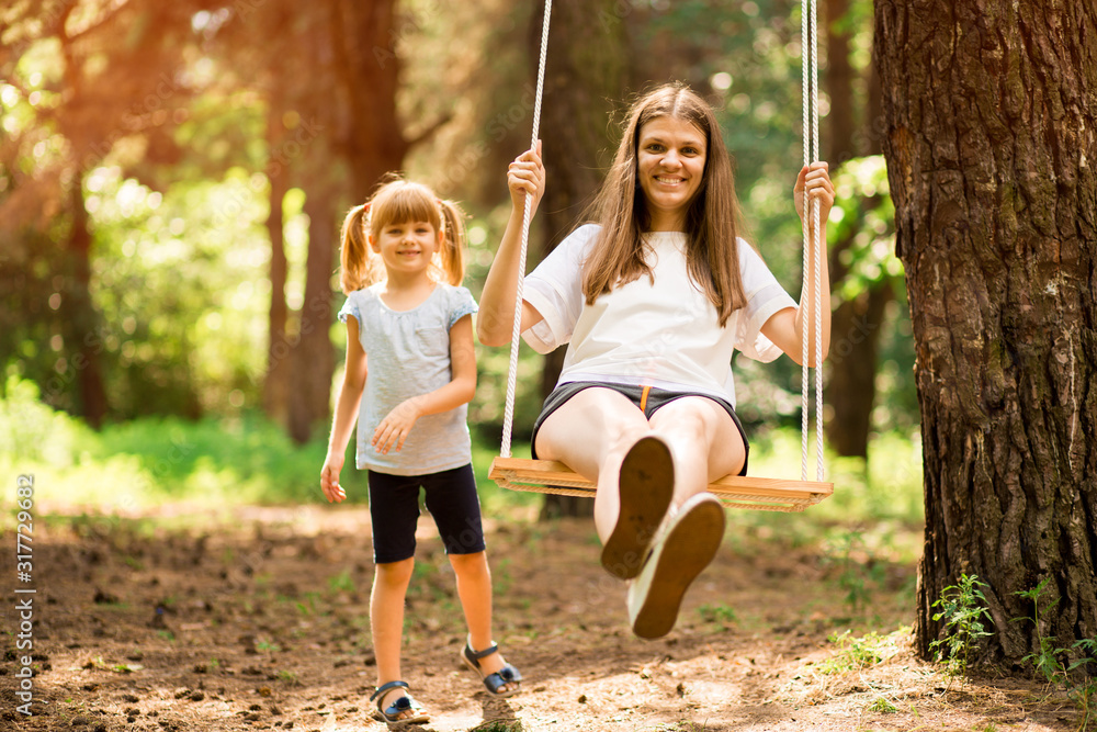happy daughter pushing laughing mother on swing in a park