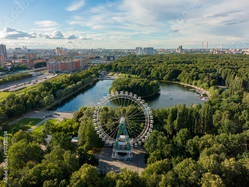 Aerial view of the Ferris wheel in the recreation park, beautiful summer nature and a large pond in the frame, urban recreation area.