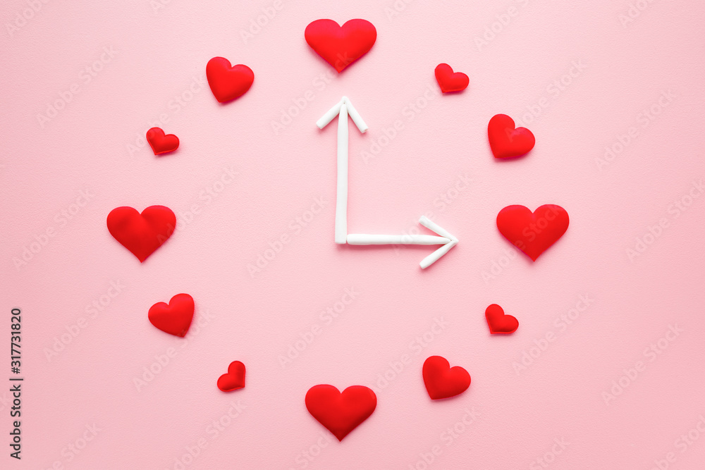 Clock created from bright red hearts and white arrows on light pink table background. Dating time. Love concept. Closeup. Flat lay.