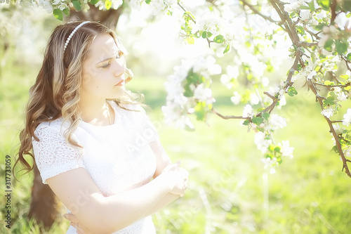 light portrait of an apple tree, girl portrait of a high key, spring mood freshness and purity blonde with long hair in a blooming park in the spring
