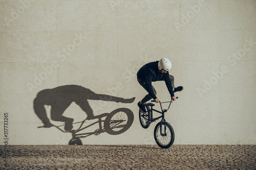 Bmx flatland rider doing a spin with his shadow projected in a stone wall