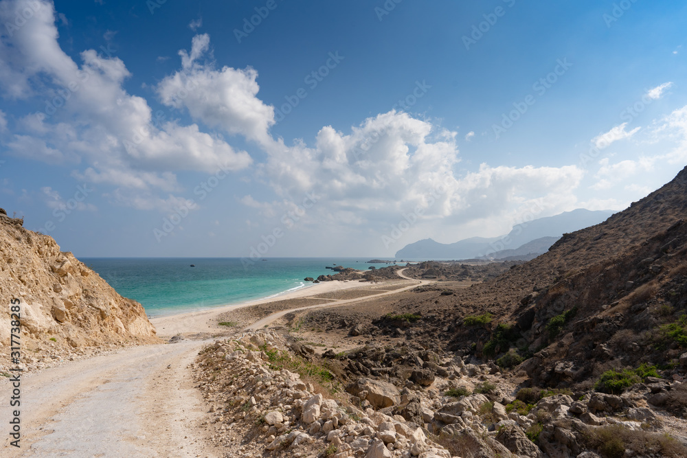 sandy path to lonely Fazayah Beach, Salalah Oman, Fantastic seascape, great outdoor scene of Beauty of nature concept background, blue sea, few clouds, light sandy beach, mountains, offroad