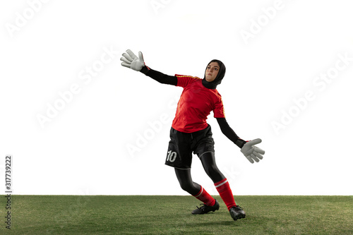 Arabian female soccer or football player, goalkeeper on white studio background. Young woman catching ball, training, protecting goals in motion and action. Concept of sport, hobby, healthy lifestyle.