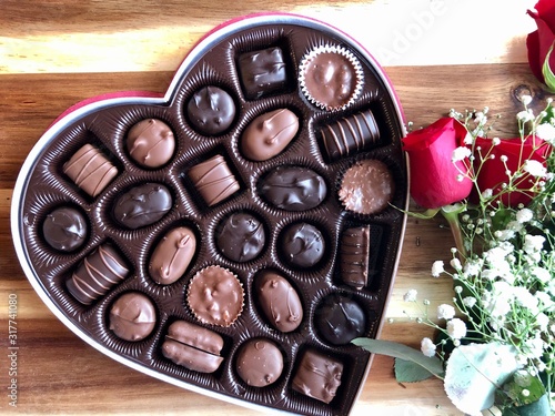 heart shaped box of valentine's day chocolates and a bouquet of red roses on a wooden table