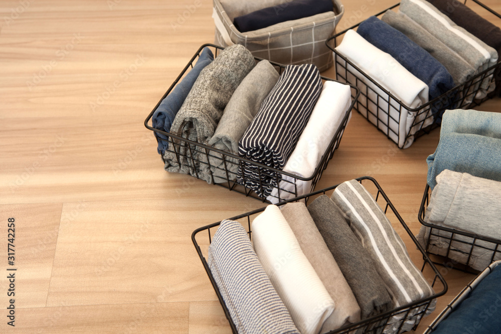 Vertical tidying up storage. Neatly folded clothes neutral colors in the metal black baskets for wardrobe. Wooden background. Nordic style.