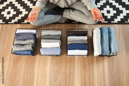 Vertical tidying up storage. Neatly folded clothes neutral colors in the metal black baskets for wardrobe. Wooden background. A woman is meditating. photo