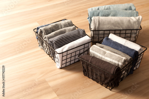 Vertical tidying up storage. Neatly folded clothes neutral colors in the metal black baskets for wardrobe. Wooden background. Nordic style. photo