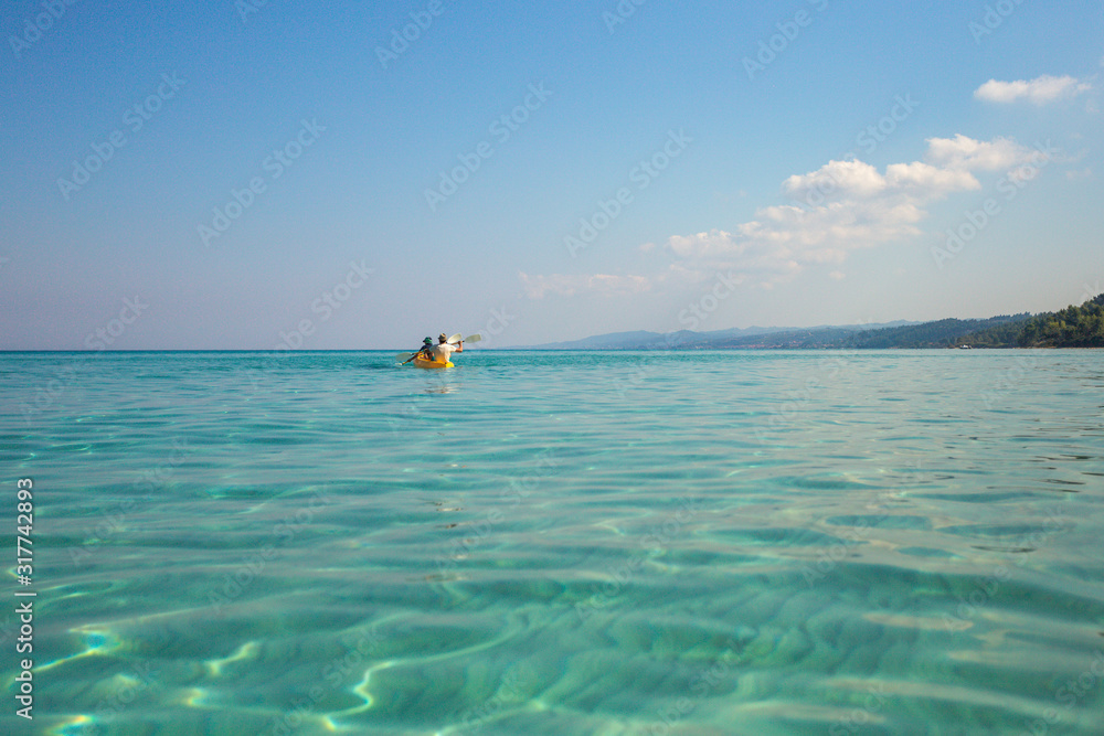 Father and son kayaking together in amazing beautiful blue water of Aegean sea in Greece. Happy summer beach holidays and travel adventures concept. Horizontal color photography.