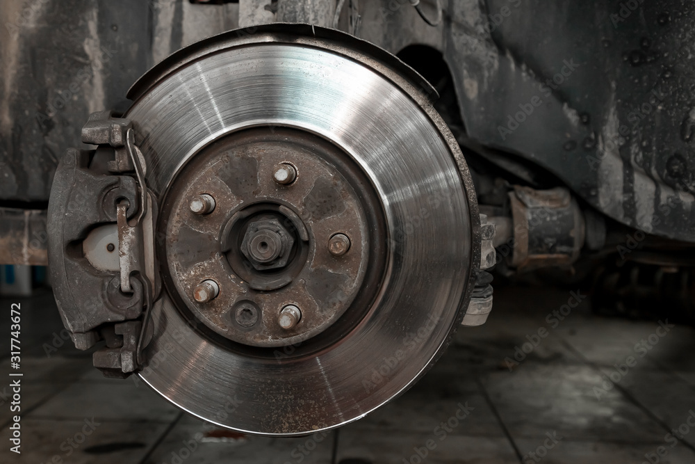 The braking system of the car with the wheel removed with the disc, pads, silver hub during maintenance and replacement in the workshop on the vehicle repair. Auto service industry.